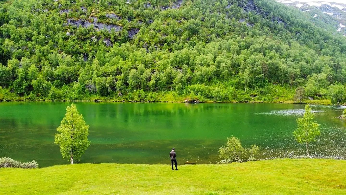A lone traveller beside a green lake in the Norwegian mountains